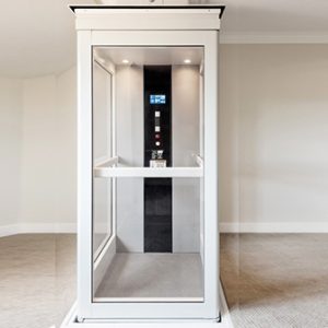 How Much Does A Home Elevator Cost. It's Interior view of a modern home elevator with glass walls and control panel.