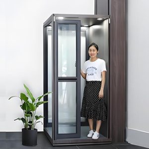 A woman standing inside a hydraulic home elevator with glass panels and a modern design.