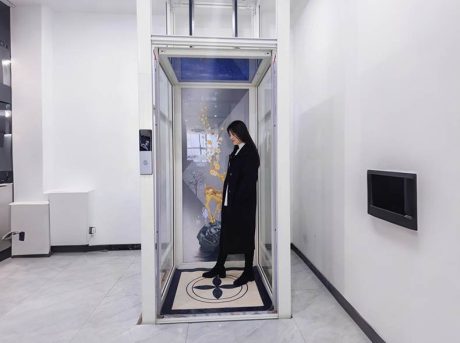 a modern white elevator for home use, with a lady stand inside the cabin platform. 