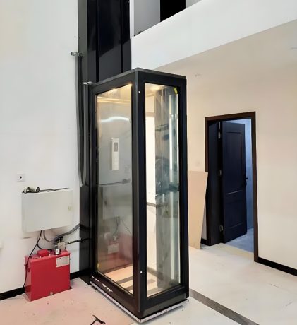 A glass residential lift installed in a modern interior space with a black frame.