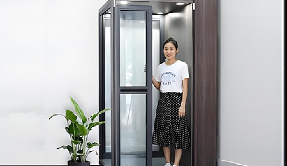 A woman standing inside a hydraulic home elevator with glass panels and a modern design.